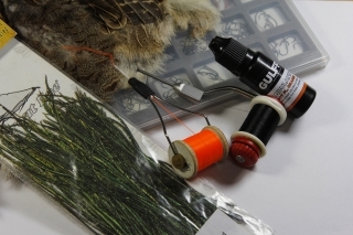 Materiály: 
pupový háčik, pierka z jarabice, čierna viazacia niť, oranžová viazacia niť, pierko z chvosta páva, oranžový UV lak.